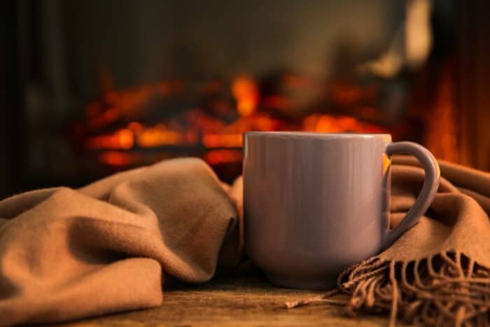 Cup with hot drink and blanket on table against fireplace Cup with hot drink and blanket on table against fireplace
